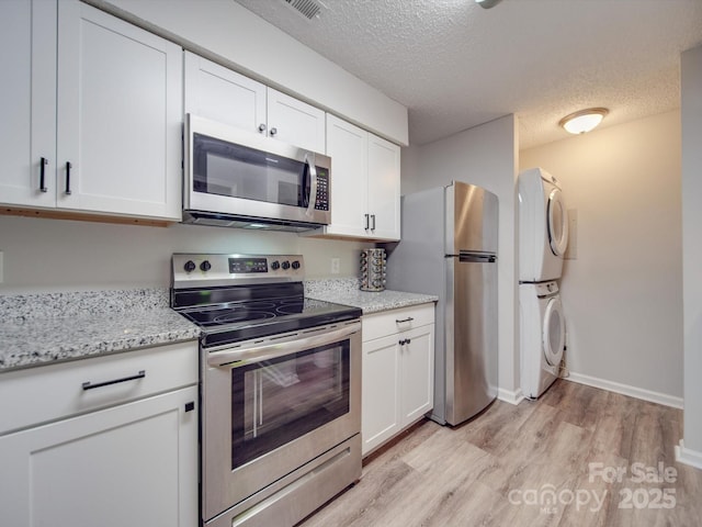 kitchen featuring stacked washer and clothes dryer, white cabinetry, a textured ceiling, light hardwood / wood-style flooring, and appliances with stainless steel finishes