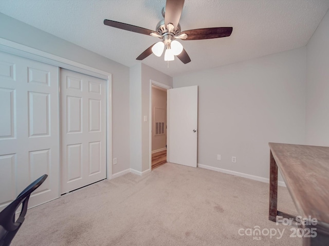 unfurnished bedroom with light carpet, ceiling fan, a closet, and a textured ceiling