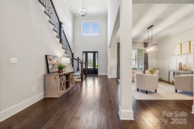 entryway featuring crown molding, dark wood-type flooring, a healthy amount of sunlight, a chandelier, and stairs