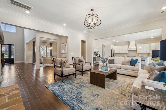 living room featuring visible vents, baseboards, wood-type flooring, ornamental molding, and a chandelier