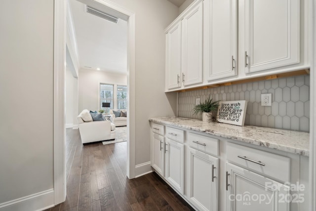 bar featuring dark wood-style flooring, visible vents, baseboards, and decorative backsplash