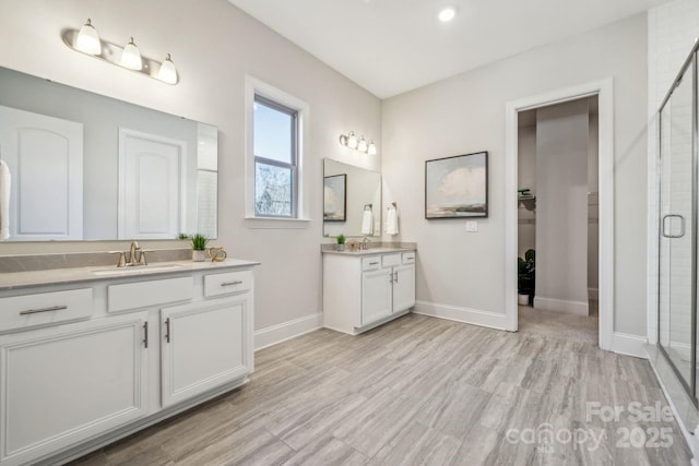 bathroom with wood finished floors, two vanities, baseboards, a sink, and a shower stall