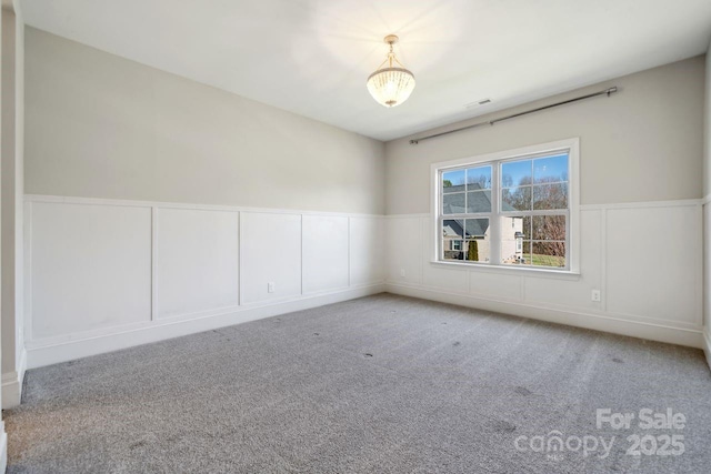 carpeted spare room with wainscoting, visible vents, and a decorative wall