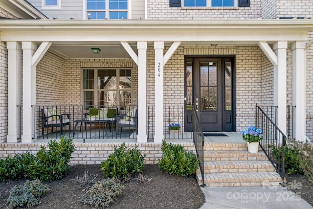 view of exterior entry featuring covered porch and brick siding