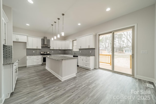 kitchen featuring wall chimney range hood, white cabinetry, hanging light fixtures, stainless steel appliances, and a center island