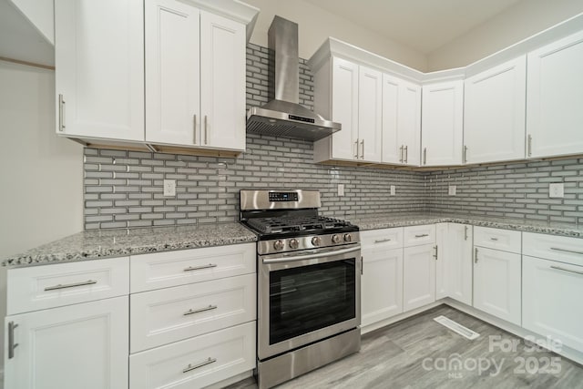 kitchen featuring white cabinetry, gas range, decorative backsplash, and wall chimney exhaust hood
