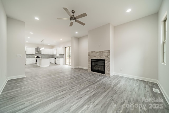 unfurnished living room with a stone fireplace, ceiling fan, and light wood-type flooring