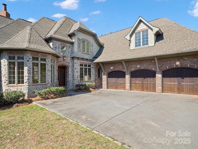 french provincial home featuring stone siding, brick siding, concrete driveway, and roof with shingles