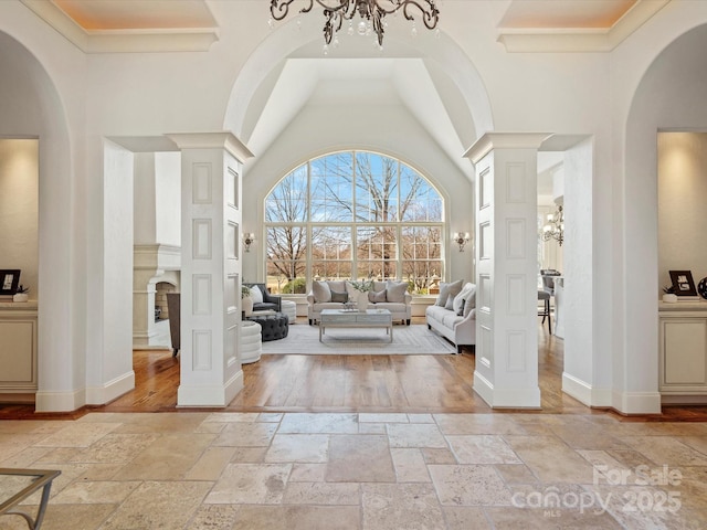 foyer entrance with stone tile floors, a towering ceiling, baseboards, an inviting chandelier, and ornate columns