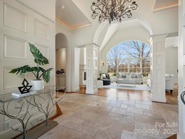 entrance foyer featuring arched walkways, stone tile flooring, decorative columns, and a towering ceiling