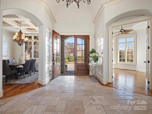 foyer featuring stone tile flooring, arched walkways, coffered ceiling, and a notable chandelier