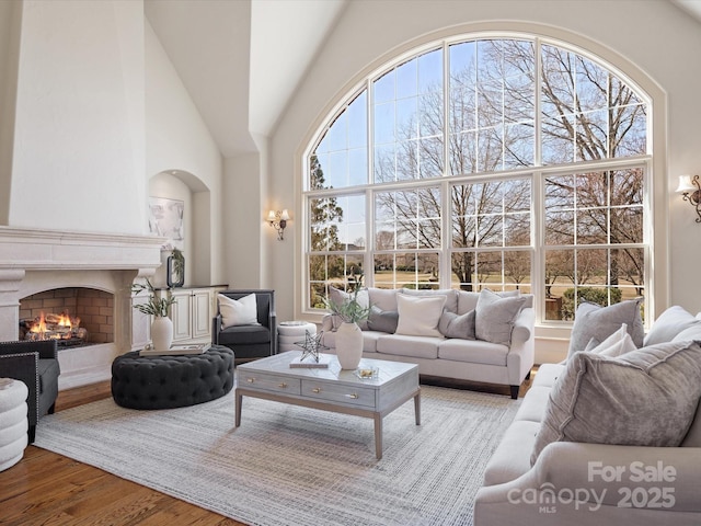 living room with a wealth of natural light, a fireplace, high vaulted ceiling, and wood finished floors