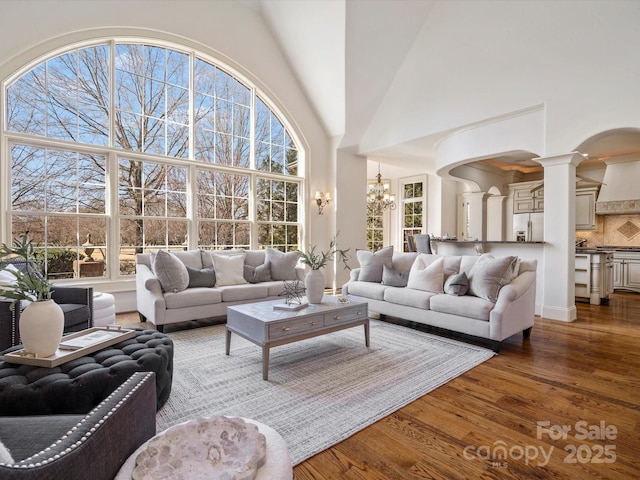 living room featuring a chandelier, decorative columns, a high ceiling, and wood finished floors