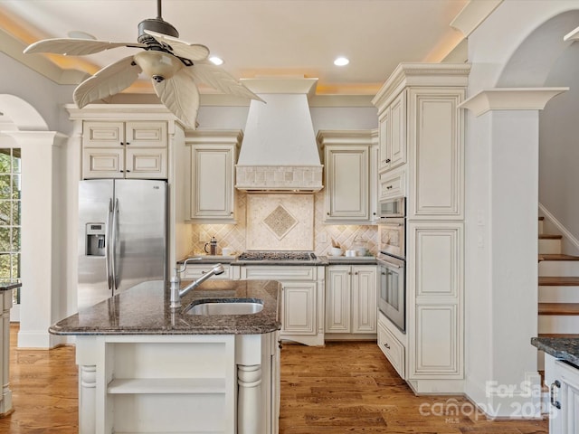 kitchen with cream cabinets, stainless steel appliances, a sink, open shelves, and custom range hood