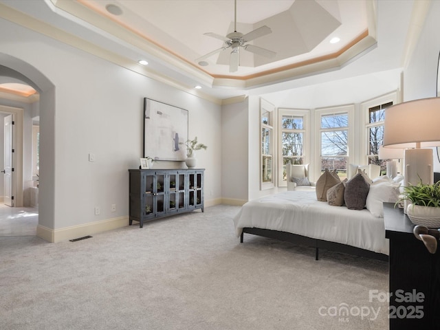 bedroom featuring arched walkways, recessed lighting, baseboards, a tray ceiling, and carpet