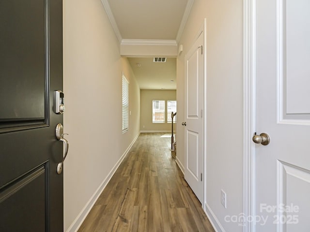 corridor featuring baseboards, visible vents, wood finished floors, and ornamental molding