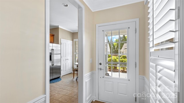 doorway with crown molding, a decorative wall, light tile patterned flooring, and a wainscoted wall