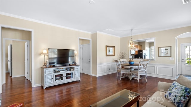 living room featuring crown molding, dark wood-style flooring, an inviting chandelier, and a wainscoted wall