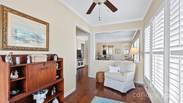 living area featuring crown molding, ceiling fan, baseboards, and dark wood finished floors