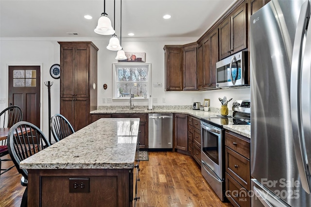 kitchen featuring decorative light fixtures, light stone countertops, a center island, and appliances with stainless steel finishes