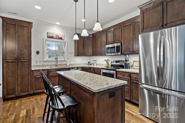 kitchen featuring a kitchen island, appliances with stainless steel finishes, decorative light fixtures, sink, and light stone countertops