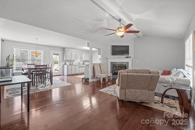 living room with a stone fireplace, vaulted ceiling with beams, sink, ceiling fan, and dark wood-type flooring