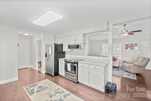 kitchen featuring ceiling fan, appliances with stainless steel finishes, white cabinetry, light stone countertops, and light hardwood / wood-style floors