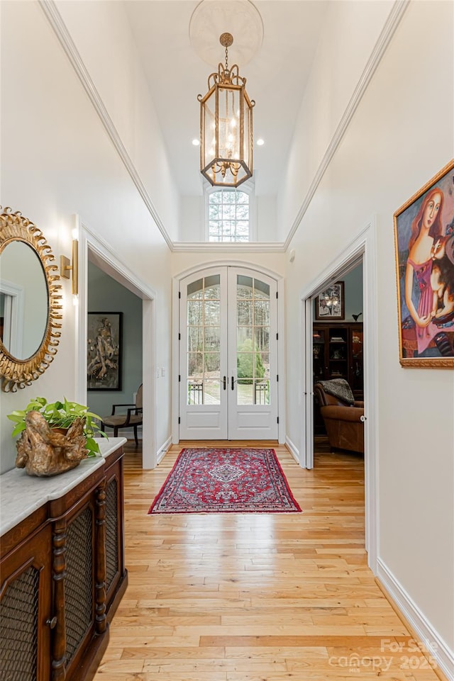 foyer entrance with a high ceiling, french doors, a chandelier, and light wood-type flooring