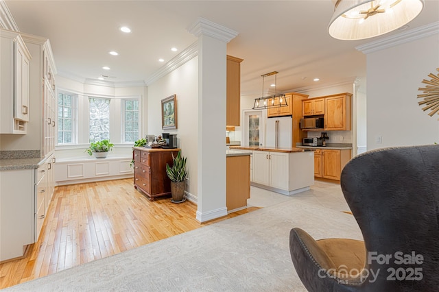 kitchen with pendant lighting, ornamental molding, high quality fridge, a kitchen island, and ornate columns