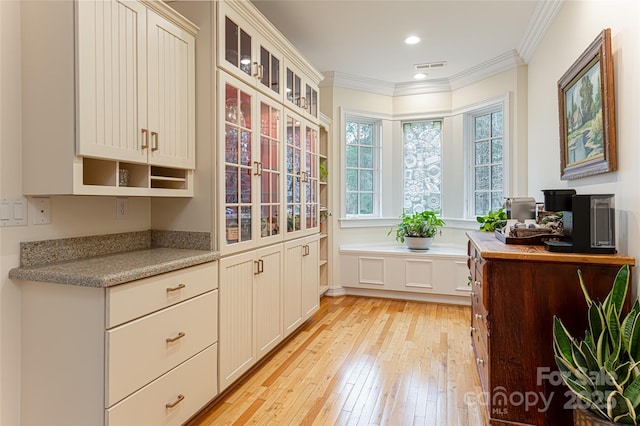 interior space featuring ornamental molding, light stone countertops, light hardwood / wood-style flooring, and white cabinets