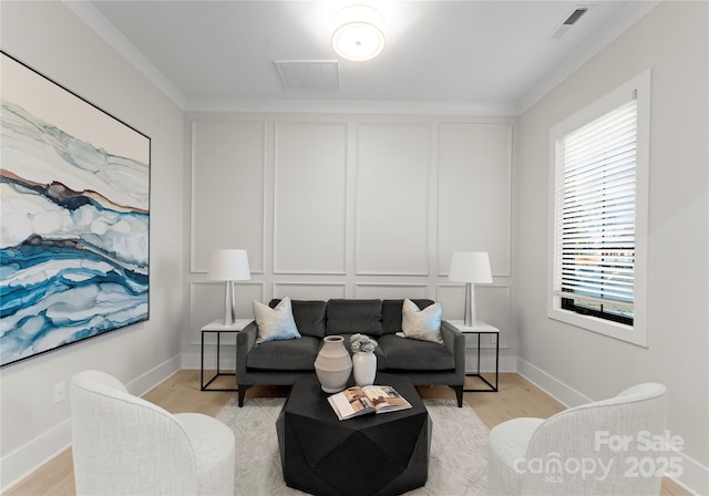 living area featuring ornamental molding, visible vents, a decorative wall, and light wood-style flooring