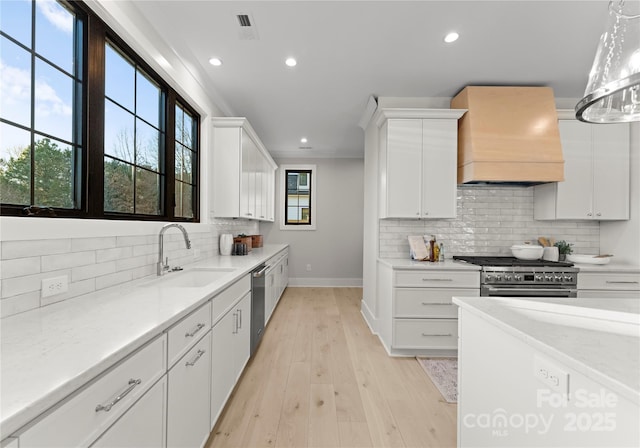 kitchen featuring stainless steel appliances, custom range hood, decorative light fixtures, and white cabinetry