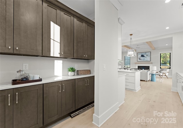 kitchen featuring light wood-style flooring, a fireplace, light countertops, dark brown cabinets, and decorative light fixtures