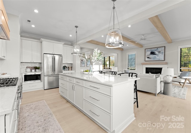 kitchen featuring appliances with stainless steel finishes, open floor plan, a kitchen island with sink, white cabinetry, and pendant lighting