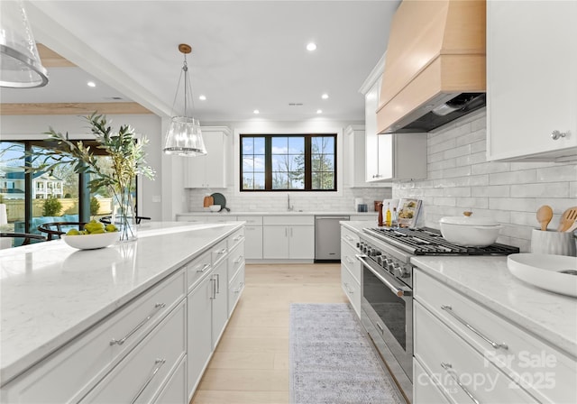 kitchen featuring light stone counters, premium range hood, white cabinets, hanging light fixtures, and appliances with stainless steel finishes