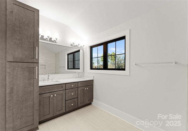 full bath featuring lofted ceiling, double vanity, baseboards, and a sink