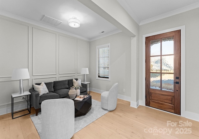 living area with ornamental molding, plenty of natural light, visible vents, and a decorative wall