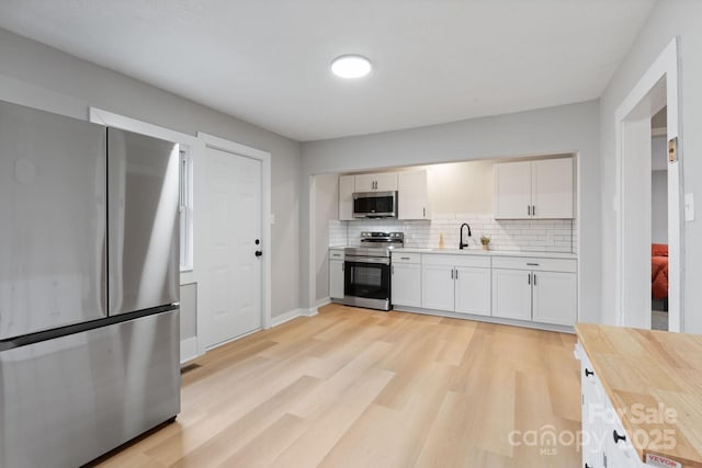 kitchen with sink, light wood-type flooring, appliances with stainless steel finishes, decorative backsplash, and white cabinets