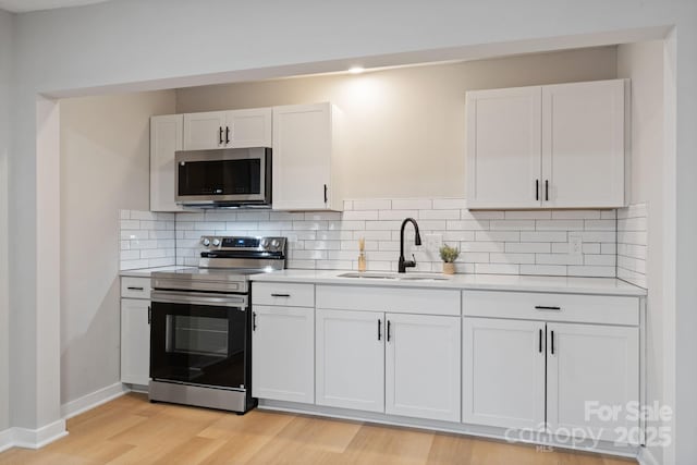 kitchen with sink, white cabinetry, tasteful backsplash, stainless steel appliances, and light hardwood / wood-style floors