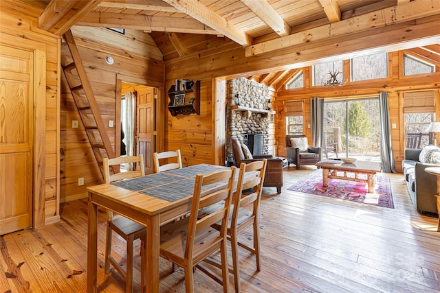 dining room featuring light wood-style flooring, a fireplace, wood walls, and lofted ceiling with beams