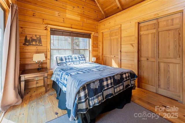 bedroom with light wood finished floors, a closet, wood ceiling, vaulted ceiling, and wooden walls