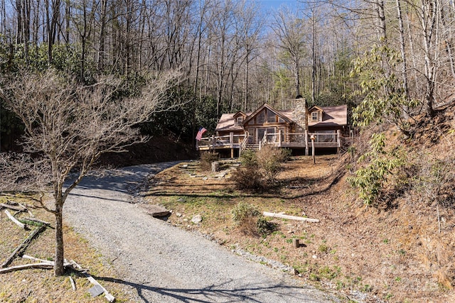 view of front of home with gravel driveway, a chimney, and a wooden deck