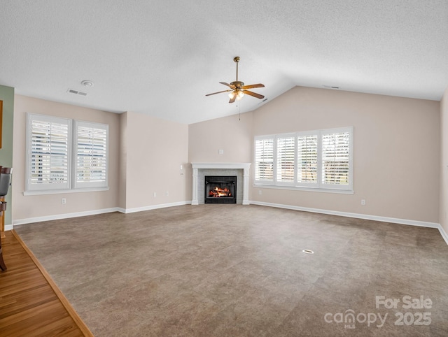 unfurnished living room featuring visible vents, a warm lit fireplace, baseboards, ceiling fan, and vaulted ceiling