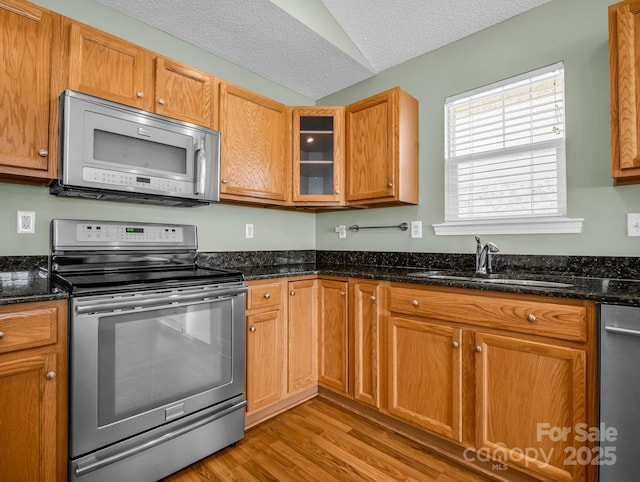 kitchen featuring a sink, dark stone countertops, a textured ceiling, stainless steel appliances, and light wood finished floors