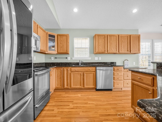 kitchen featuring plenty of natural light, appliances with stainless steel finishes, glass insert cabinets, and light wood-style floors