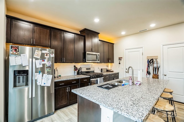 kitchen featuring a kitchen bar, sink, light stone counters, a center island with sink, and appliances with stainless steel finishes