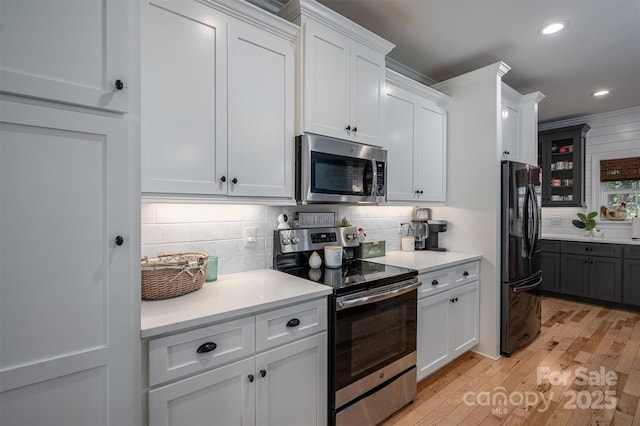 kitchen with light wood-type flooring, appliances with stainless steel finishes, white cabinetry, and decorative backsplash