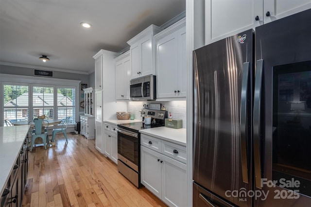 kitchen featuring white cabinets, crown molding, stainless steel appliances, and decorative backsplash