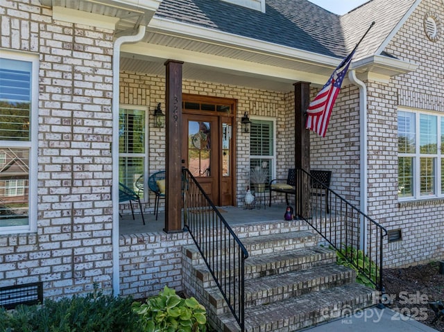 property entrance with a shingled roof, brick siding, covered porch, and crawl space