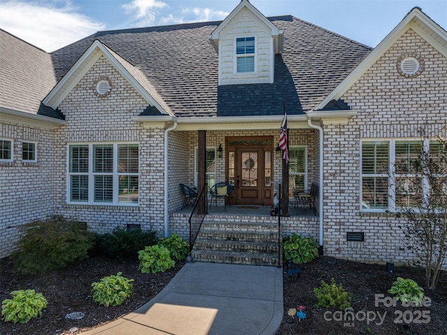 property entrance with crawl space, brick siding, a porch, and roof with shingles